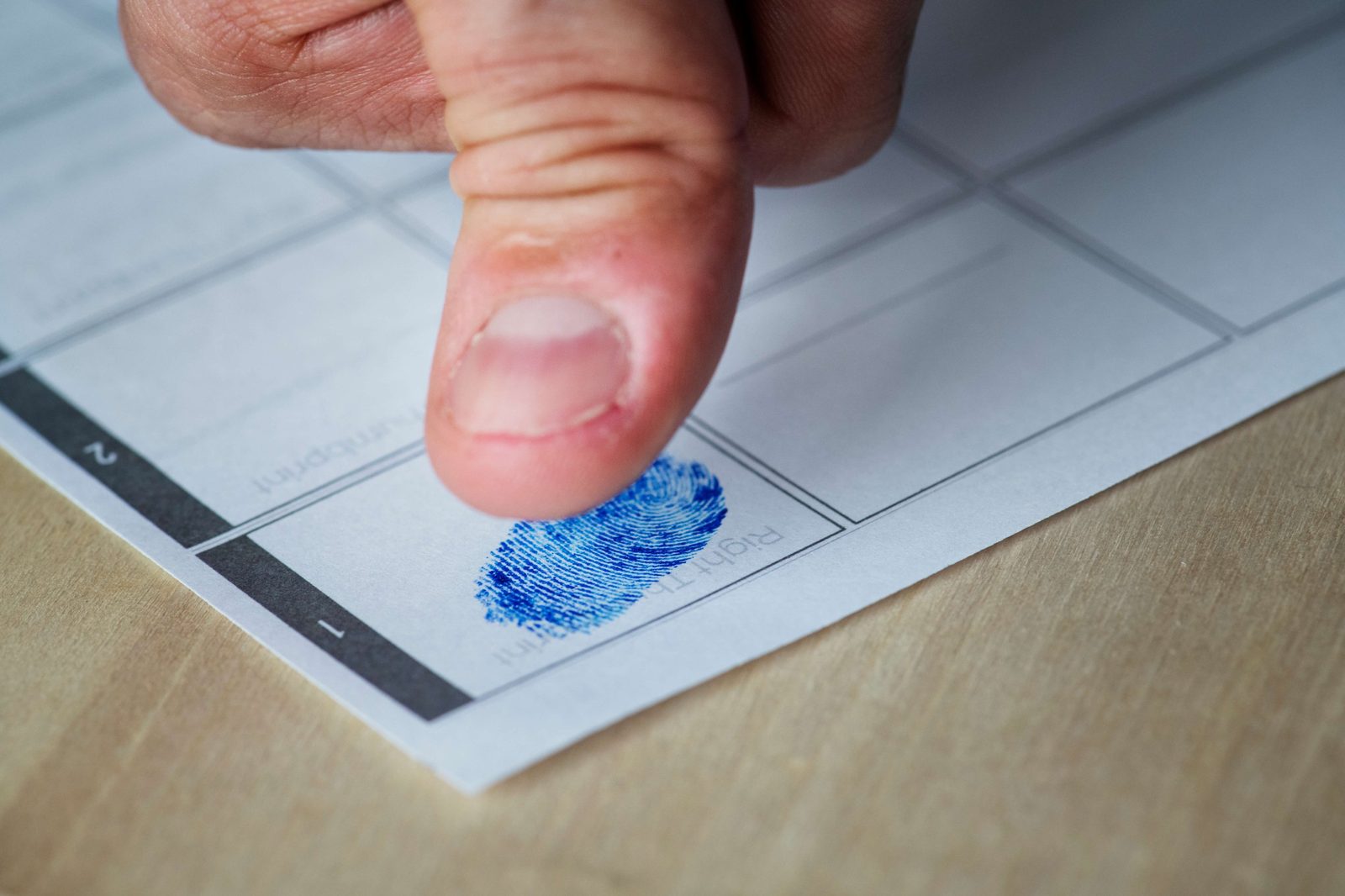 Close-up of a person fingerprinting a document with their index finger, coated with blue ink.