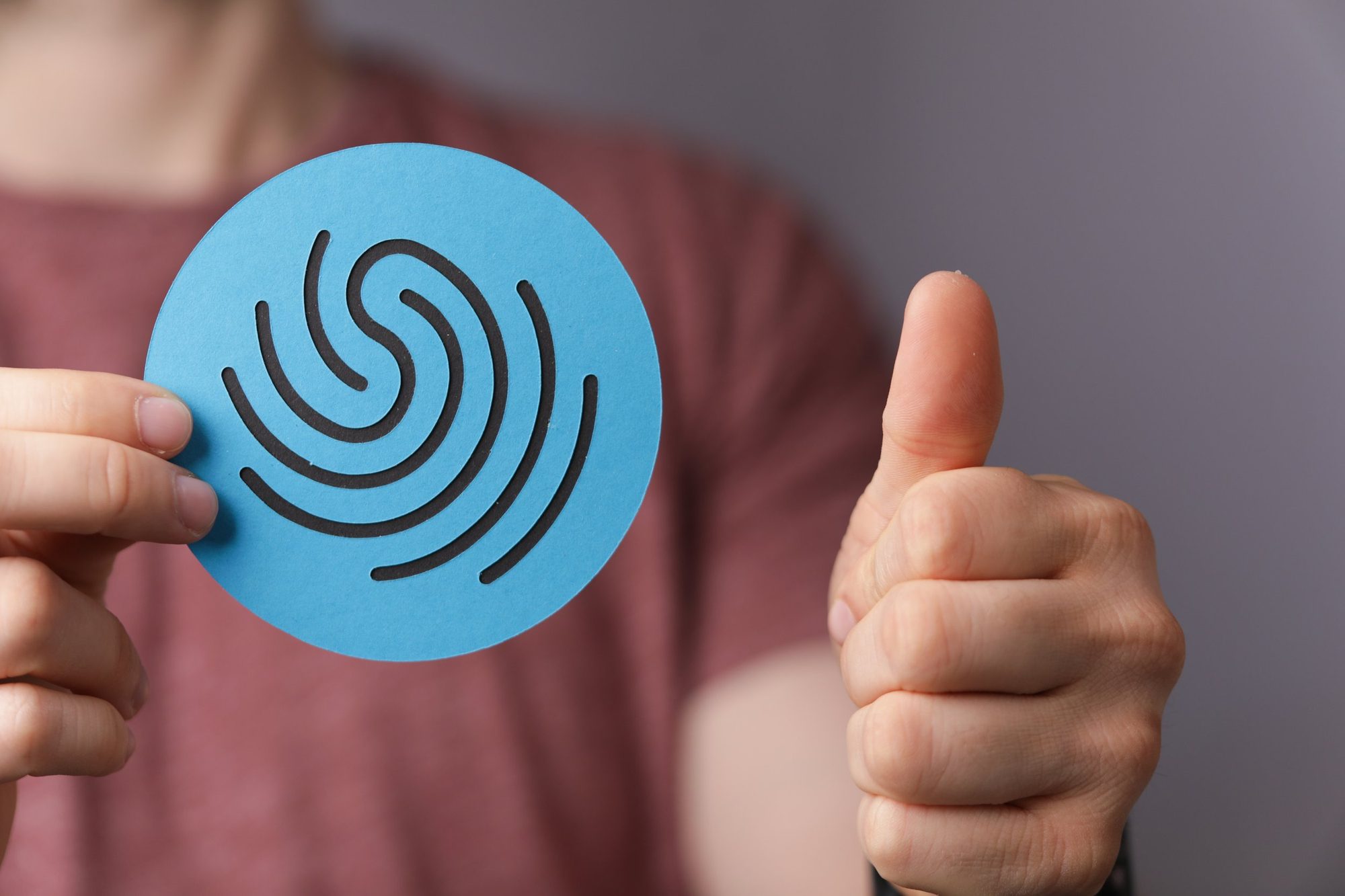 Person holding up a blue circular paper with black fingerprint pattern, giving a thumbs up.