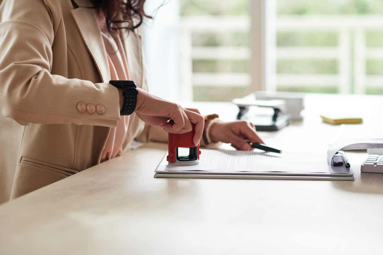 Person stamping a document with a red ink stamp, sitting at a desk near a window.